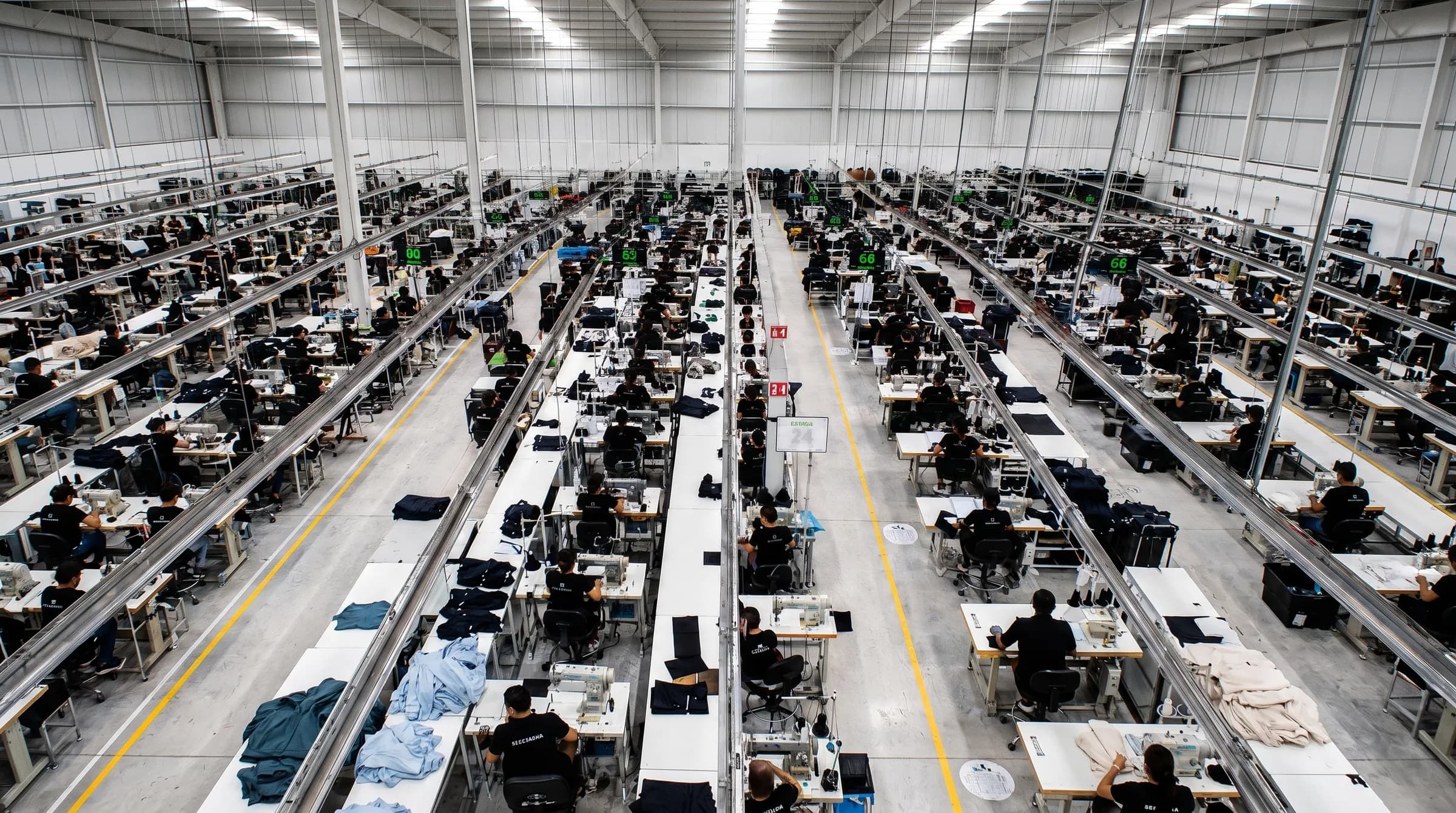 Vista elevada de un piso de confección con largas hileras de máquinas de coser y operarios trabajando
